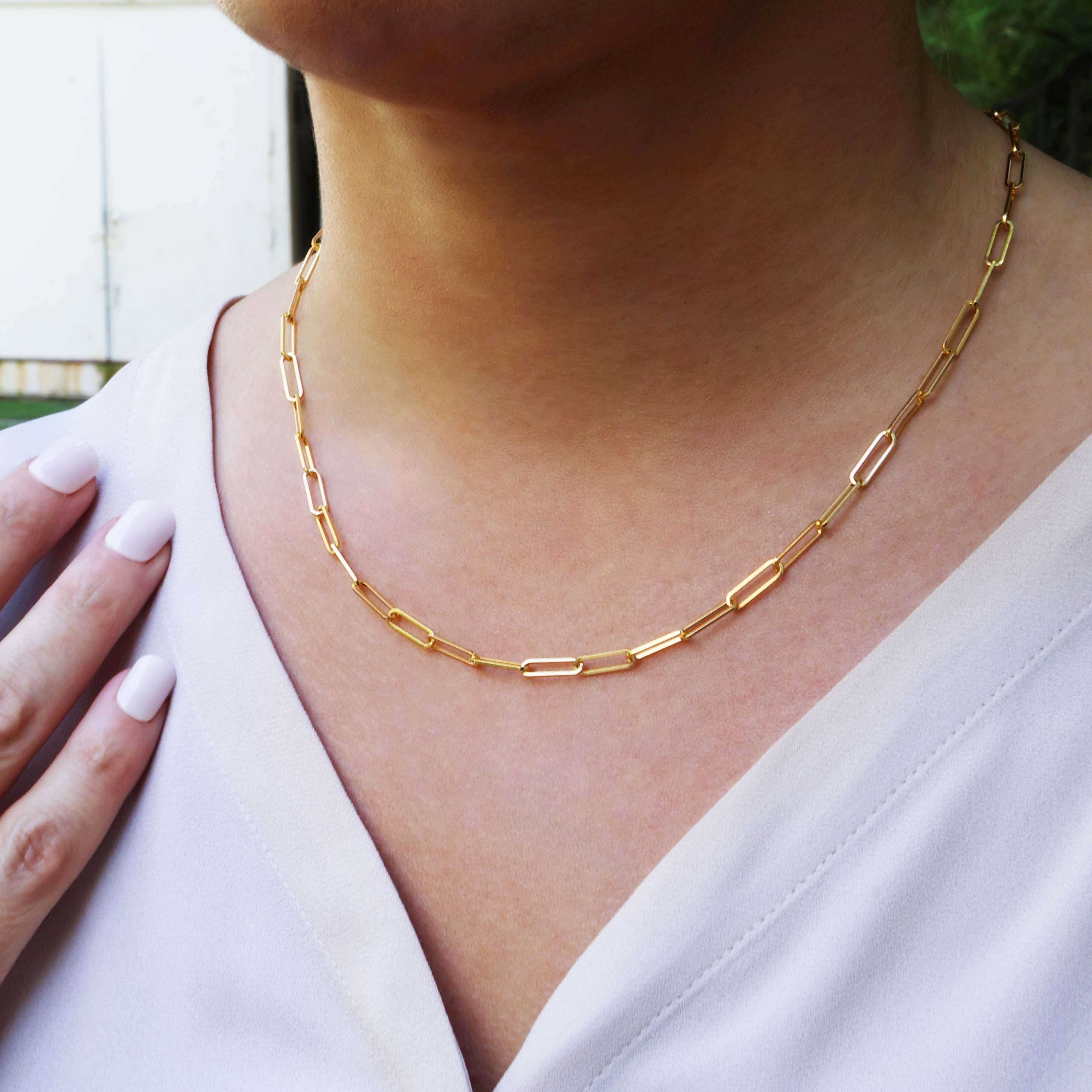 Gold chain link necklace worn by a person with a white top.