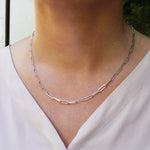 Silver chain link necklace on a person wearing a light-colored top with a blurred background