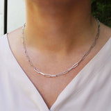 Silver chain link necklace on a person wearing a light-colored top with a blurred background