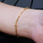 Gold chain link bracelet on a wrist against a dark background